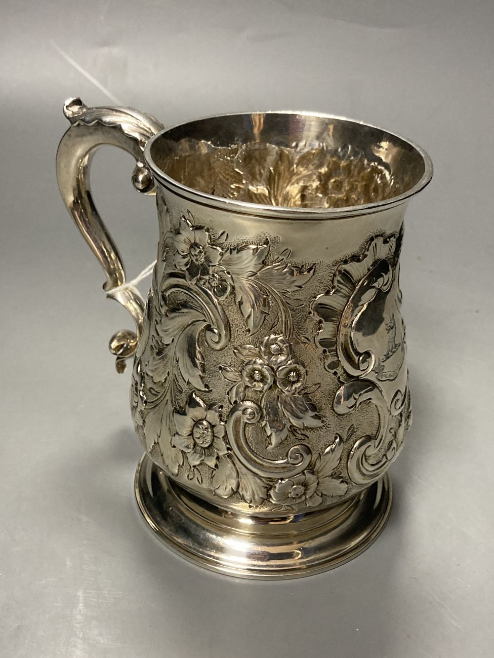 An early George III silver mug, with engraved crest and later embossed decoration, William Shaw II, London, 1764,